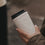 Cremefarbener To-Go-Kaffeebecher mit Herzmotiv und schwarzem Deckel in einer Hand