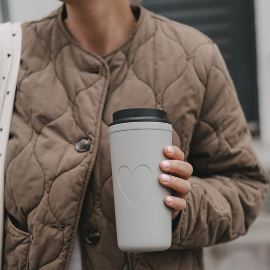 Grauer To-go-Thermobecher mit Herzmotiv in der Hand einer Frau