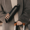 Frau hält eine schwarze Trinkflasche mit Herzmotiv in der Hand und zieht mit der anderen einen Koffer.