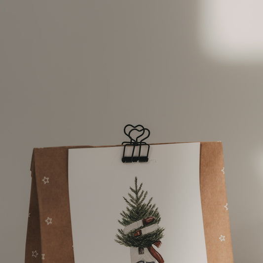 Nahaufnahme eines schwarzen Foldback-Clips mit Herzmotiv, der eine Weihnachtskarte an einer Geschenktüte befestigt.