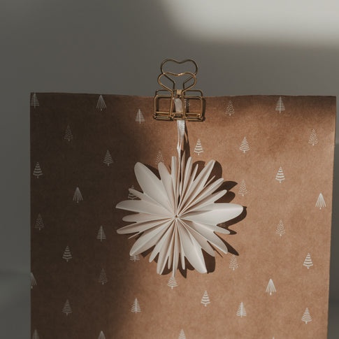 Nahaufnahme eines goldenen Herz-Clips mit weißem Papierstern als weihnachtliche Geschenkverpackung.