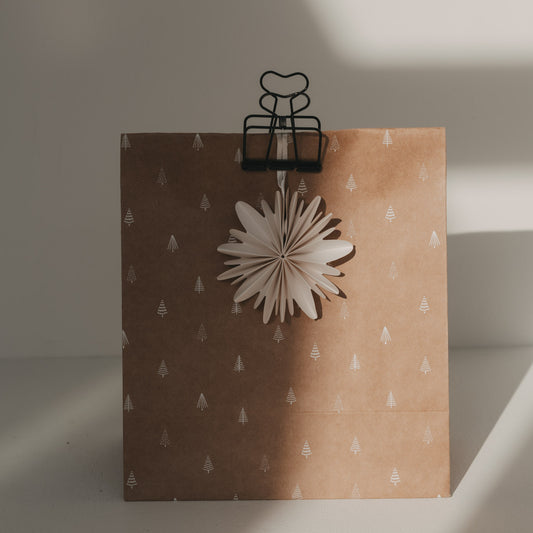 Schwarzer Herz-Clip hält eine braune Geschenktüte mit Tannenbaummuster und weißem Papierstern zusammen.