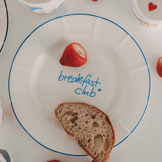 Frühstücksteller mit „breakfast club“-Schrift in Hellblau mit feinem Wellenrand – minimalistisch in Szene gesetzt mit frischer Erdbeere und Brot.