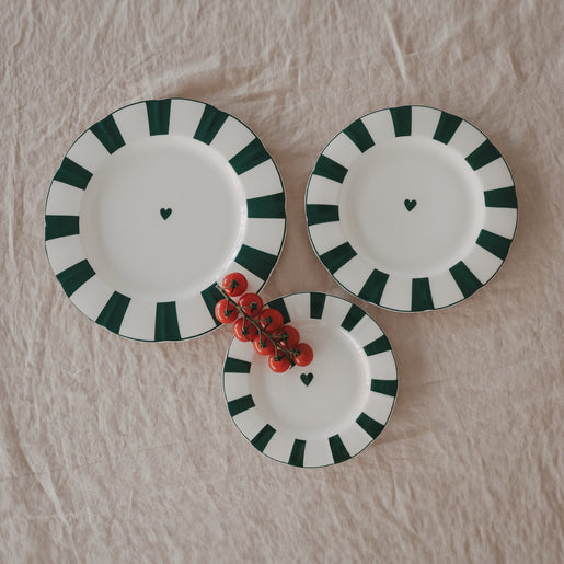 3 Porzellanteller in verschiedenen Größen mit gewelltem Rand, grünem Streifenmuster und Herzdetail, dekoriert mit frischen Tomaten auf Leinentischdecke.