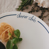 Detailansicht eines weißen „dinner club“-Tellers mit dunkelblauer Schrift und Rand, garniert mit Pasta und frischen Kräutern.