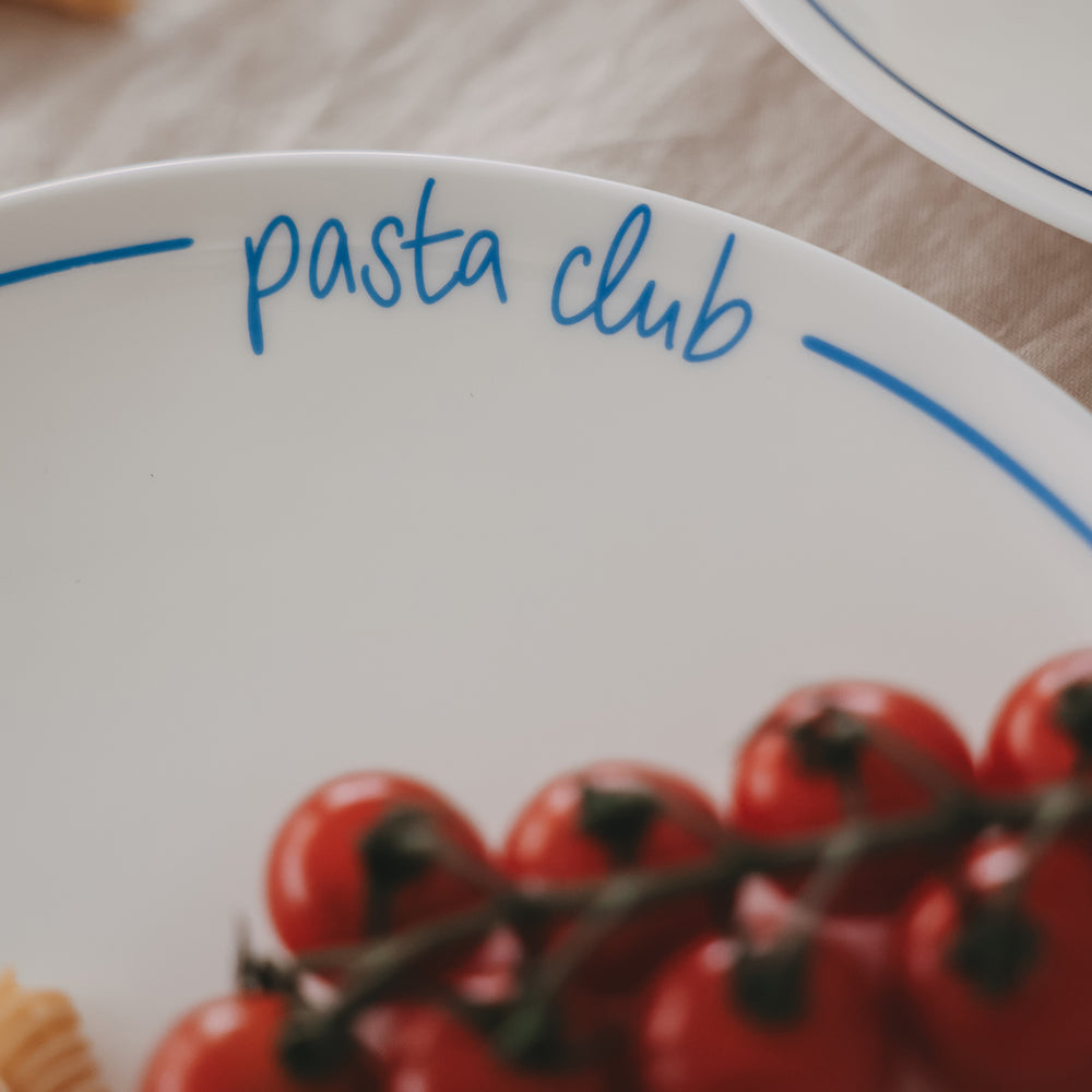 Detailaufnahme des Schriftzugs „pasta club“ auf einem weißen Speiseteller mit hellblauem Rand.