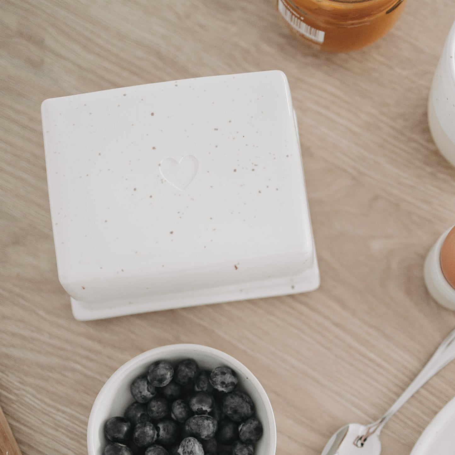 Butterdose mit Herz-Prägung aus Keramik, stilvoll inszeniert auf hellem Holztisch