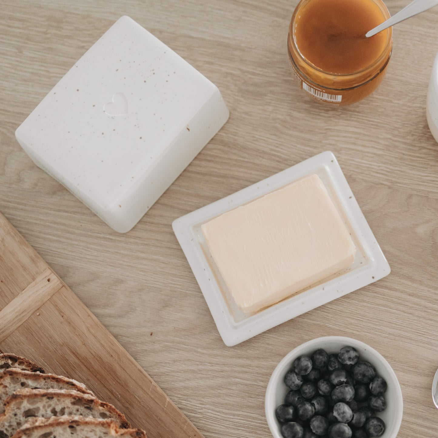 Butterdose geöffnet mit Butterstück, Keramik mit Herz auf gedecktem Frühstückstisch