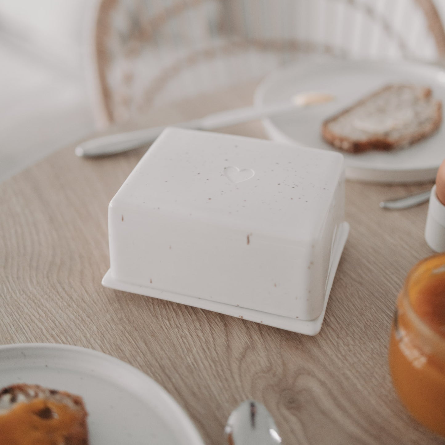 Butterdose mit Herz aus Keramik auf gedecktem Frühstückstisch mit Brot und Marmelade
