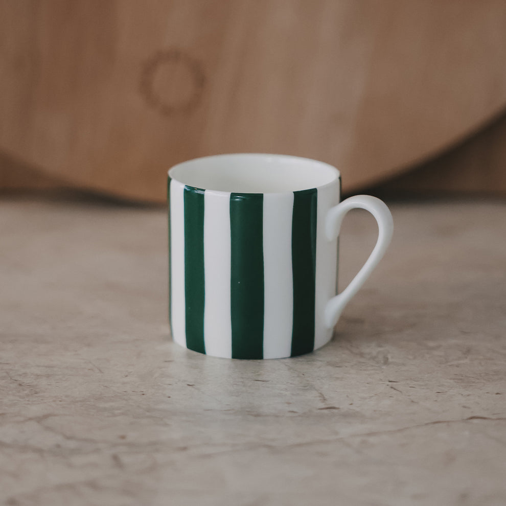 Kleine Tasse mit grünen Streifen frontal auf heller Fläche, dezenter Hintergrund mit Holzbrett.