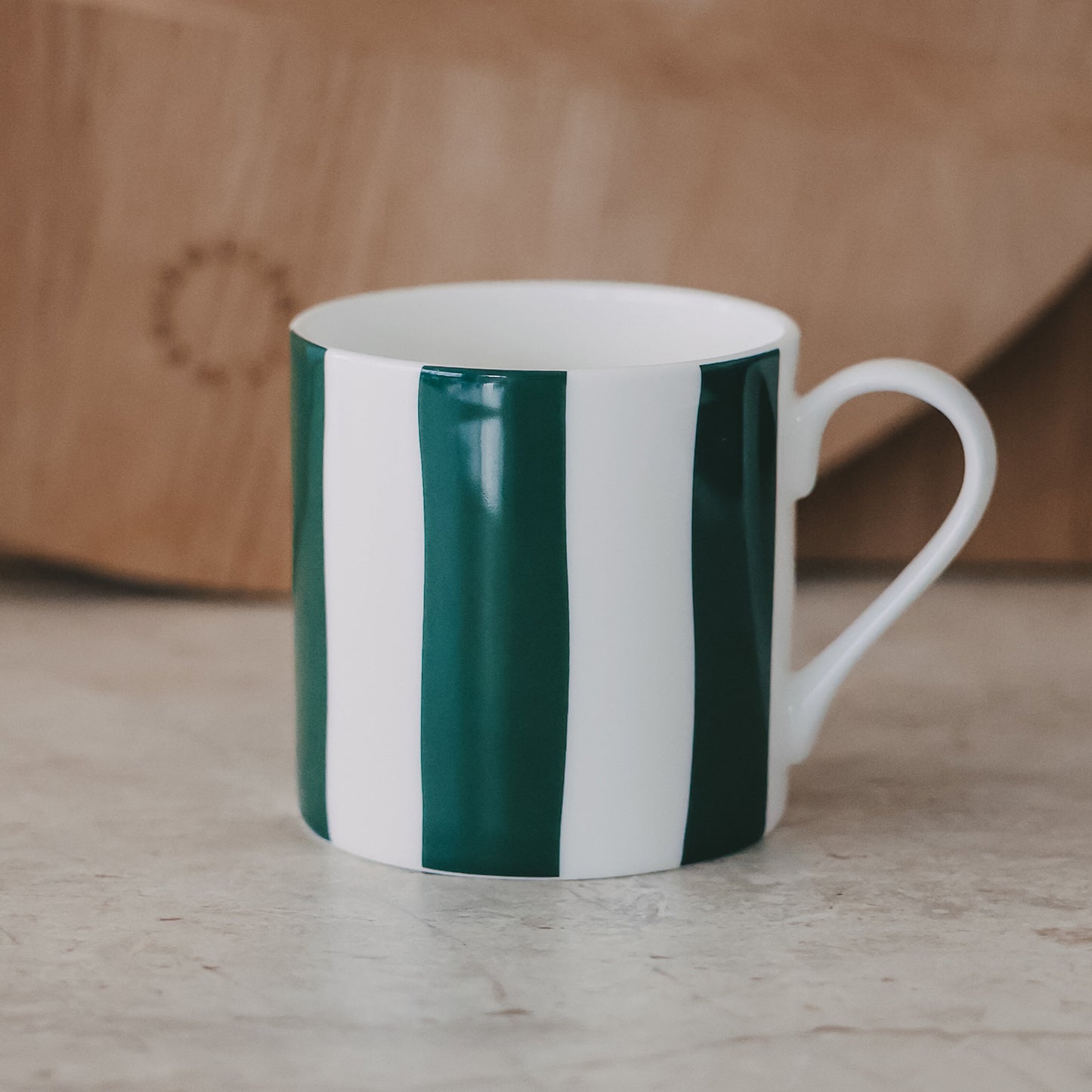 Porzellantasse mit grünen und weißen Streifen auf heller Steinoberfläche mit Holzbrett im Hintergrund