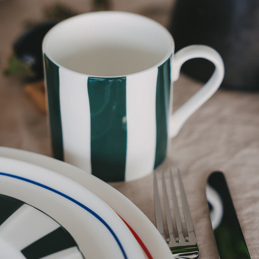 Porzellantasse mit grünen und weißen Streifen neben Teller und Besteck auf gedecktem Tisch