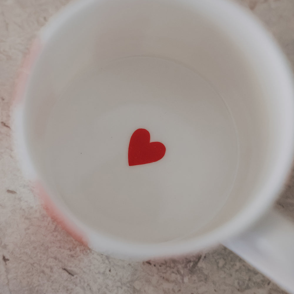 Blick in weiße Porzellantasse mit rotem Herz am Boden auf heller Steinoberfläche