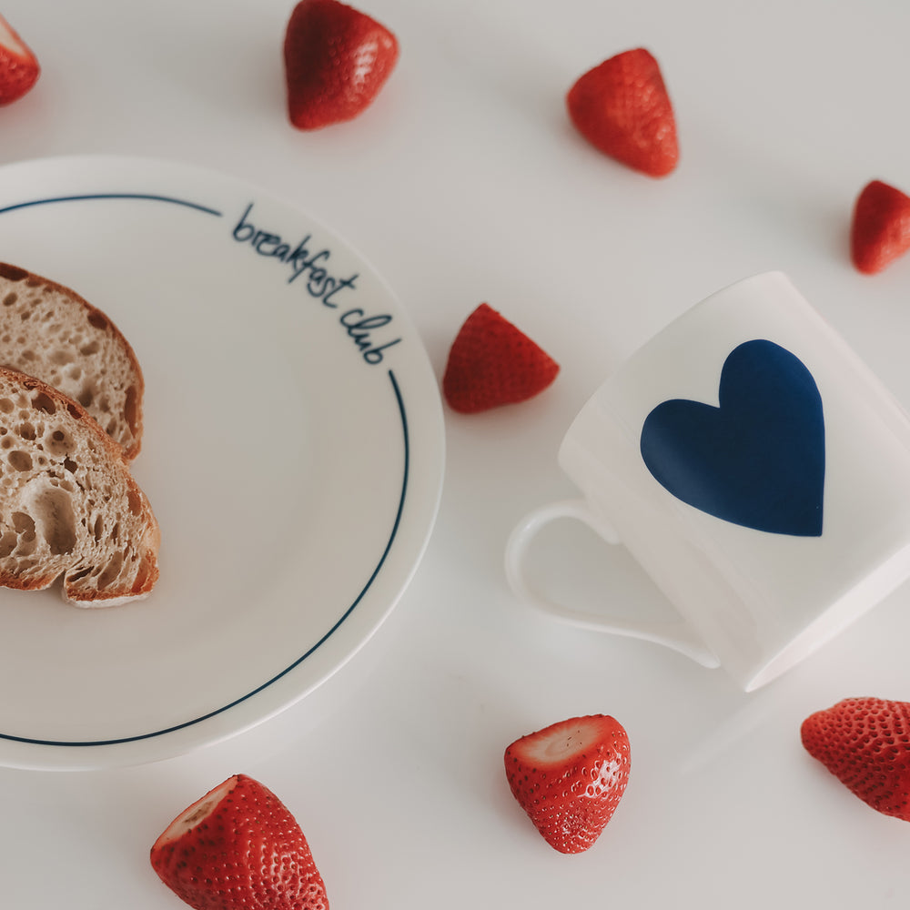 Von oben fotografierte Szene mit Teller, Brot, Erdbeeren und Tasse mit blauem Herz