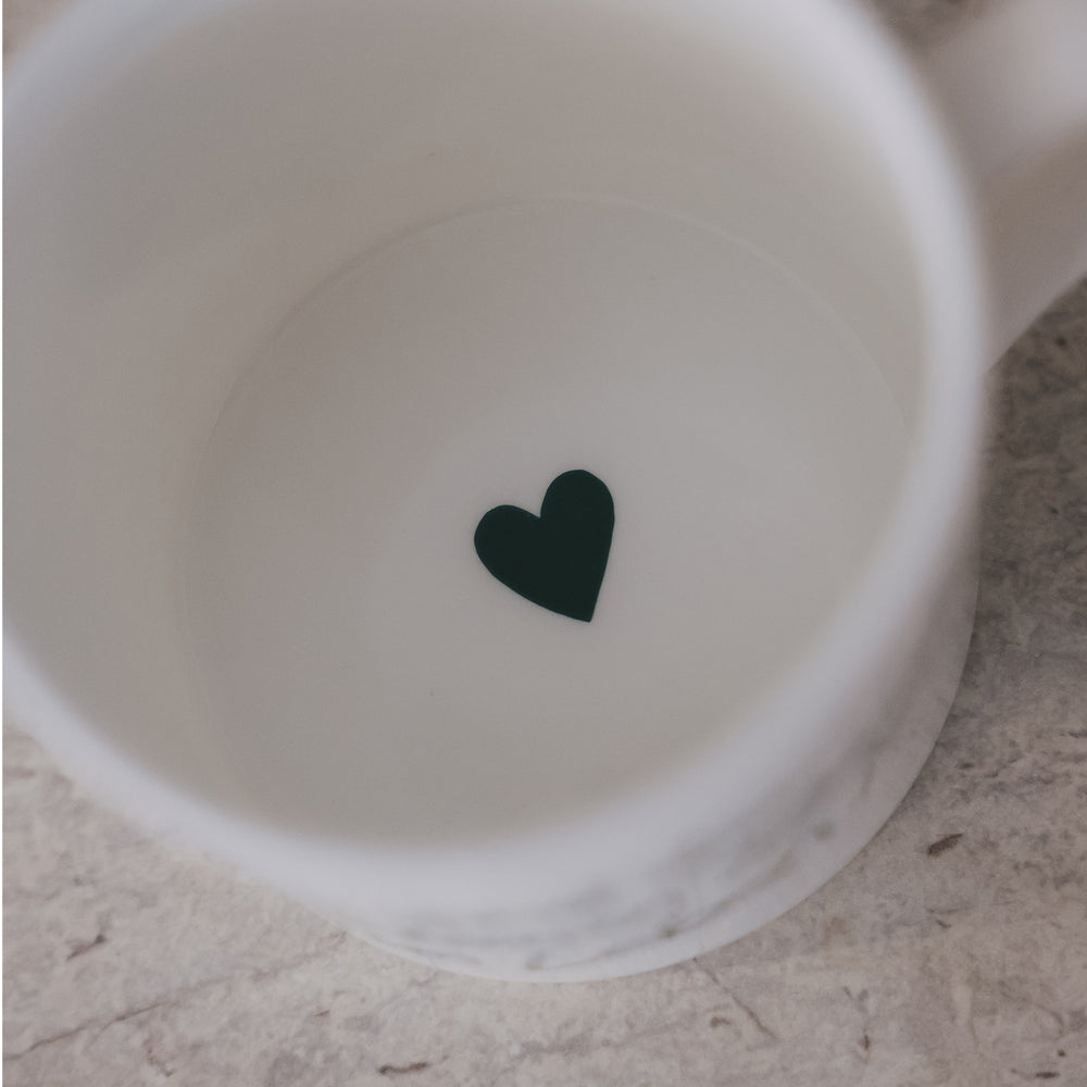 Draufsicht in eine weiße Tasse mit kleinem grünem Herz auf dem Tassenboden