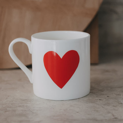 Weiße Tasse mit großem rotem Herzmotiv auf der Außenseite vor schlichtem Hintergrund