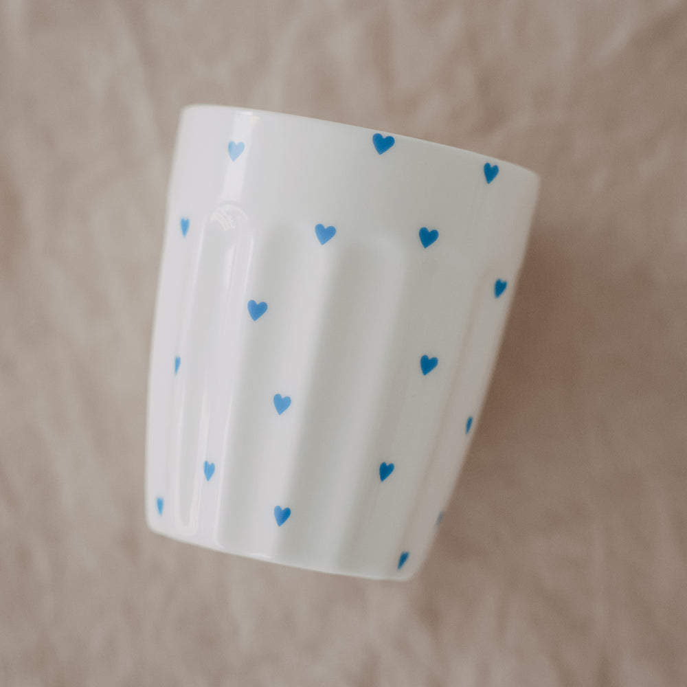 Weißer Becher mit blauen Herzen vor hellem Hintergrund