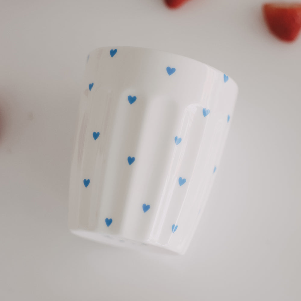 Weißer Becher mit blauen Herzen, ästhetisch inszeniert mit Erdbeeren
