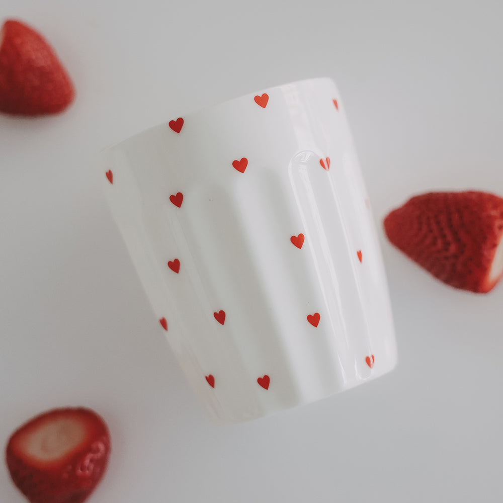Weißer Becher mit roten Herzen zwischen Erdbeeren, stilvolle Food-Fotografie