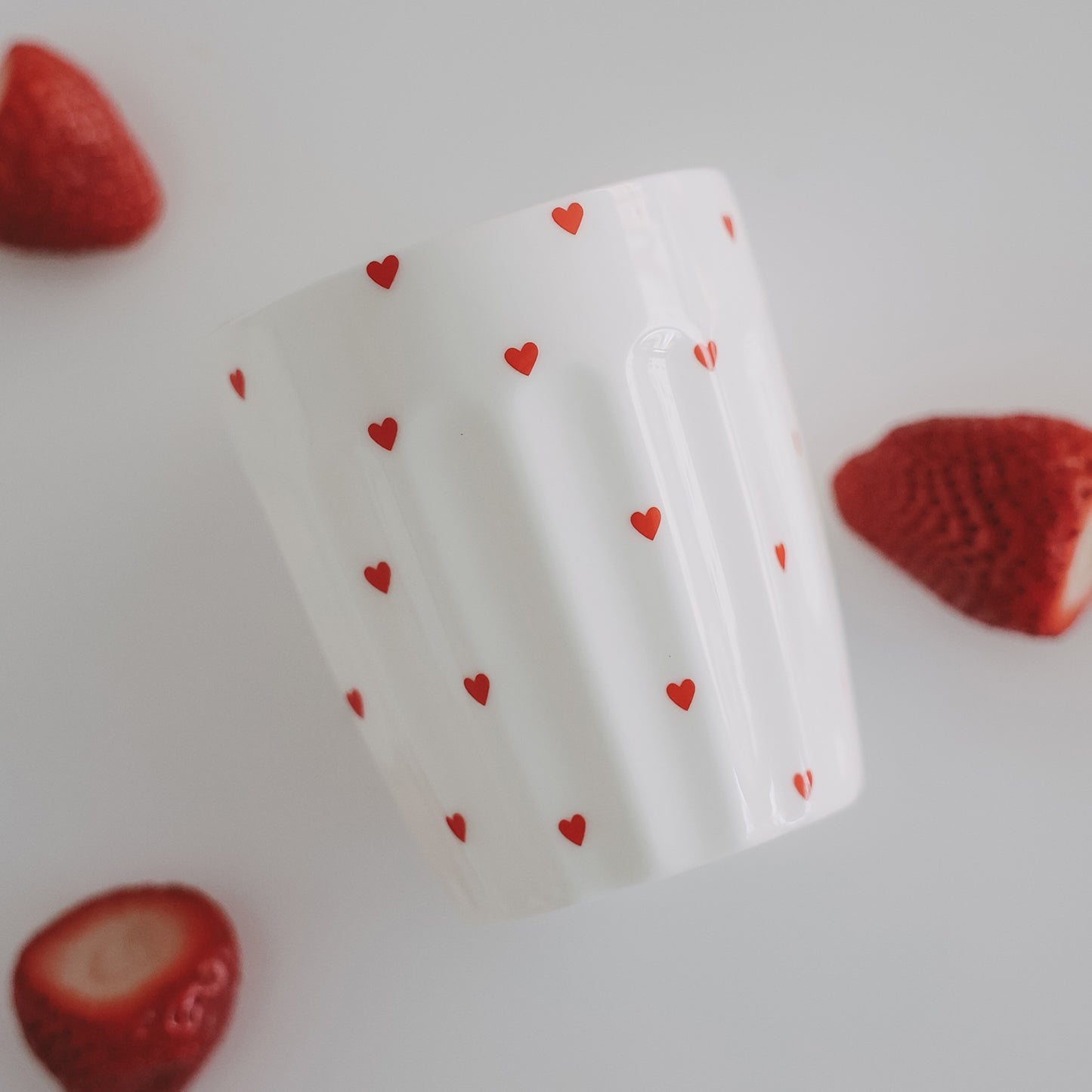 Weißer Becher mit roten Herzen zwischen Erdbeeren, stilvolle Food-Fotografie