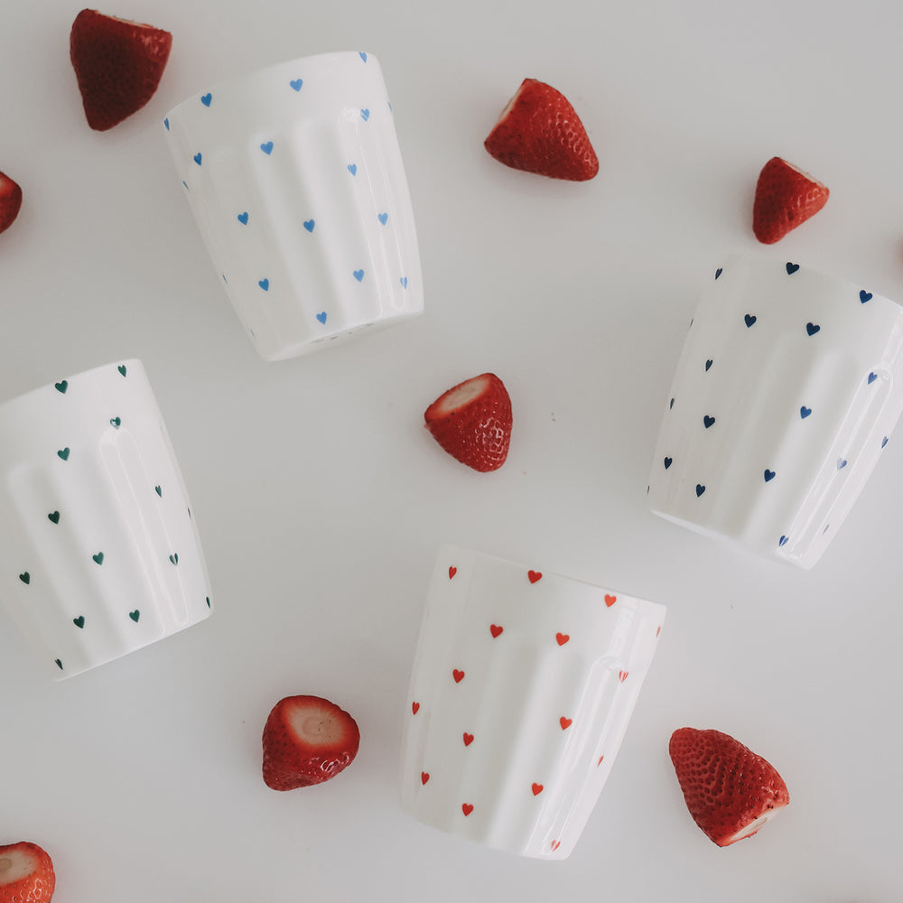 Vier Keramikbecher mit bunten Herzen und Erdbeeren, stilvolle Flatlay-Komposition