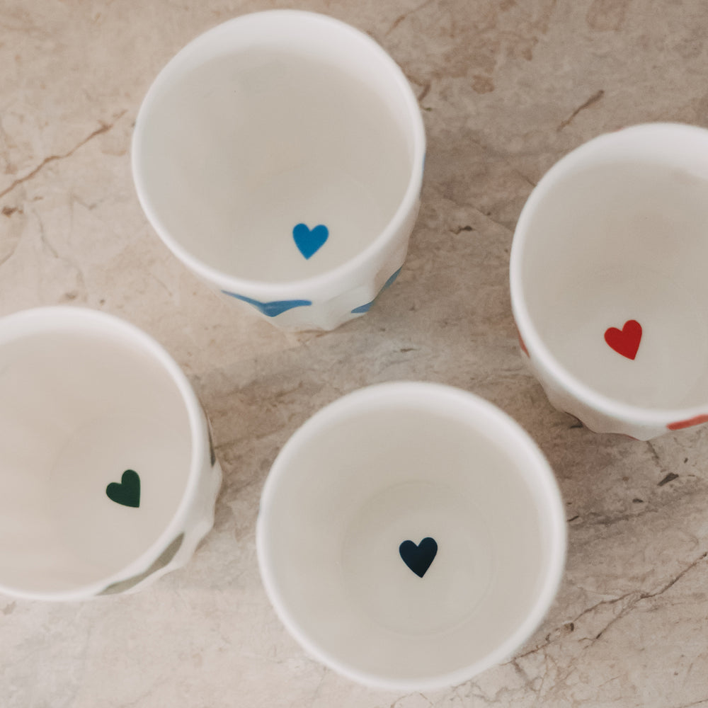 Vier Keramikbecher mit bunten Herzmotiven von oben, dekorativ angeordnet