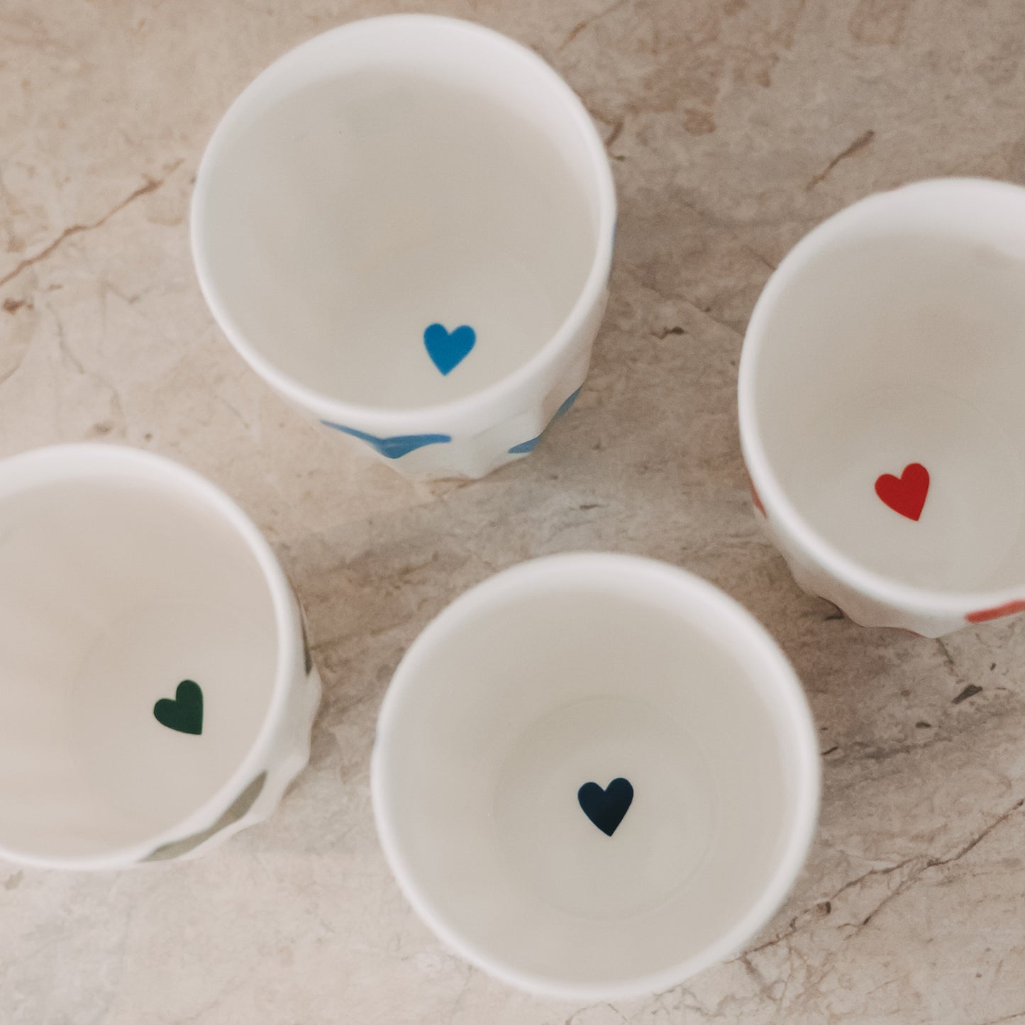 Vier Keramikbecher mit bunten Herzmotiven von oben, dekorativ angeordnet