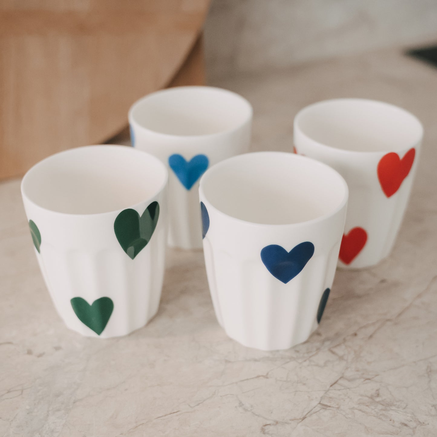 Vier Keramikbecher mit bunten Herzmotiven dekorativ auf Tisch arrangiert