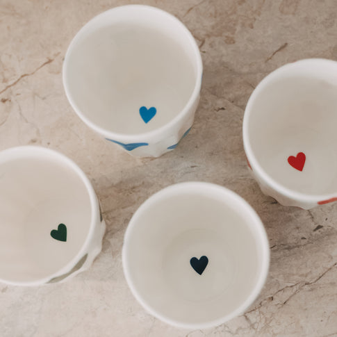 Innenansicht von Keramikbechern mit kleinen Herzmotiven am Boden in verschiedenen Farben