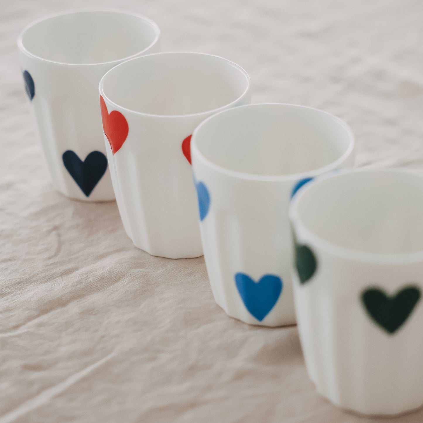 Keramikbecher mit Herzmotiven in Reihe auf Stoffuntergrund, minimalistisches Design