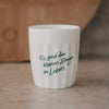 Weißer Keramikbecher mit Spruch „Es sind die kleinen Dinge im Leben“ in Grün auf natürlichem Untergrund