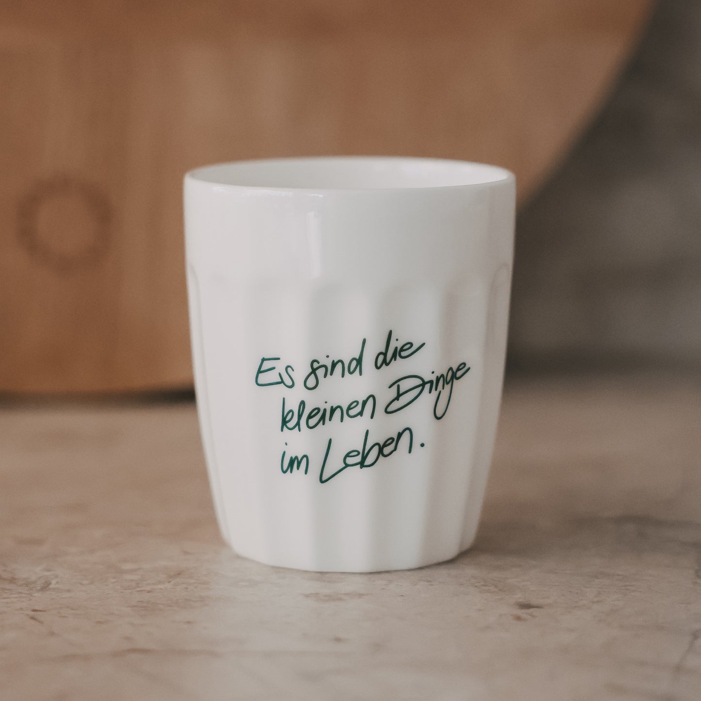 Weißer Keramikbecher mit Spruch „Es sind die kleinen Dinge im Leben“ in Grün auf natürlichem Untergrund