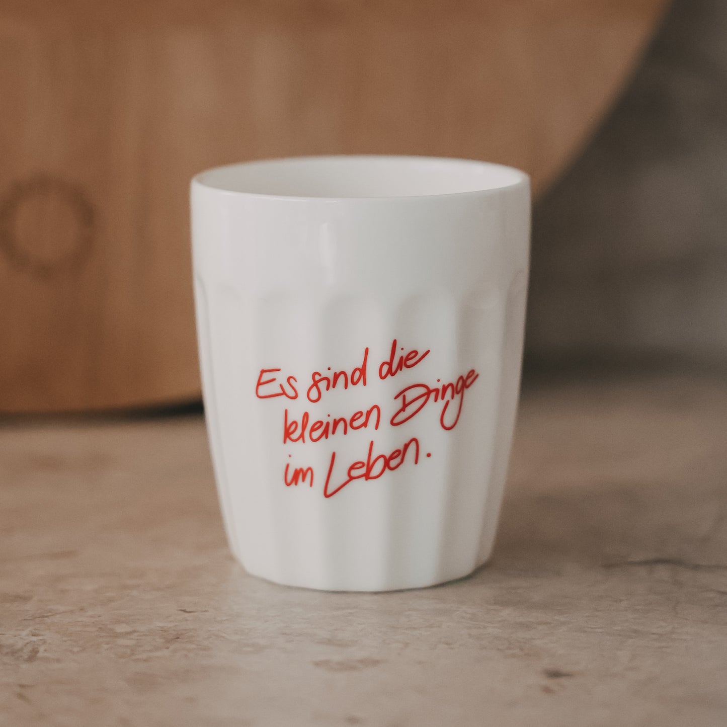 Weißer Keramikbecher mit rotem Schriftzug „Es sind die kleinen Dinge im Leben“ auf hellem Untergrund