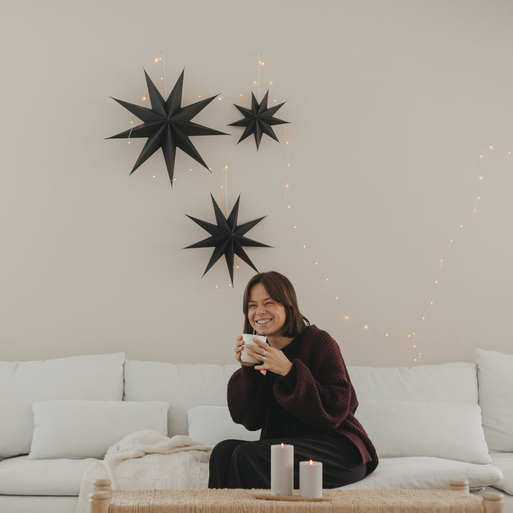Schwarze Papiersterne mit Lichterkette als minimalistische Weihnachtsdeko über weißem Sofa