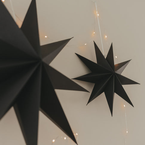 Schwarze Papiersterne mit filigranen Spitzen und warmer Lichterkette als moderne Weihnachtsdekoration