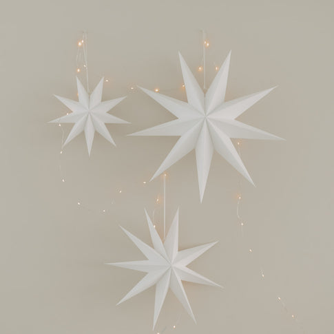 Drei weiße Papiersterne in verschiedenen Größen mit warmer Lichterkette als Weihnachtsdekoration