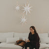 Weiße Papiersterne mit Lichterkette als minimalistische Weihnachtsdeko über einem weißen Sofa