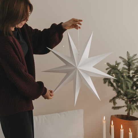 Großer weißer Papierstern mit Aufhängung neben Weihnachtsbaum und Kerzen als festliche Weihnachtsdeko