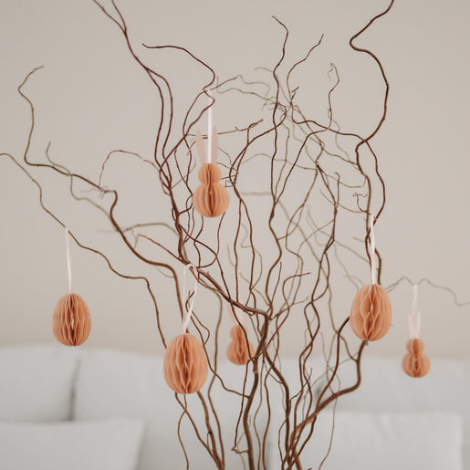 Peachfarbene Papieranhänger in Ei- und Hasenform hängen an dekorativen Zweigen.