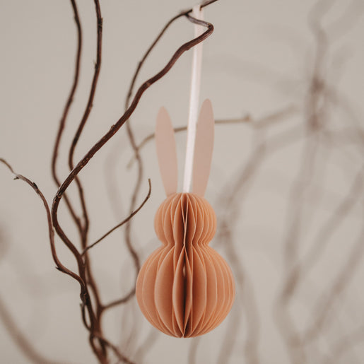 Nahaufnahme eines peachfarbenen Papieranhängers in Hasenform am Osterzweig.