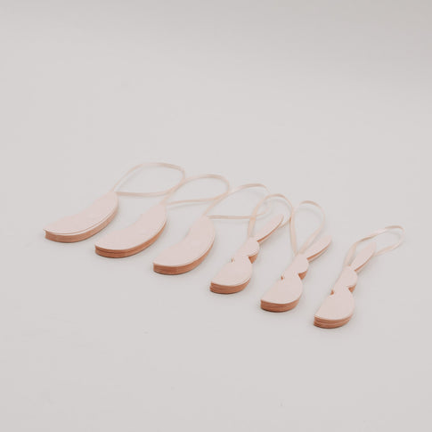 Zusammengefaltete peachfarbene Papieranhänger in Ei- und Hasenform mit Bändern.