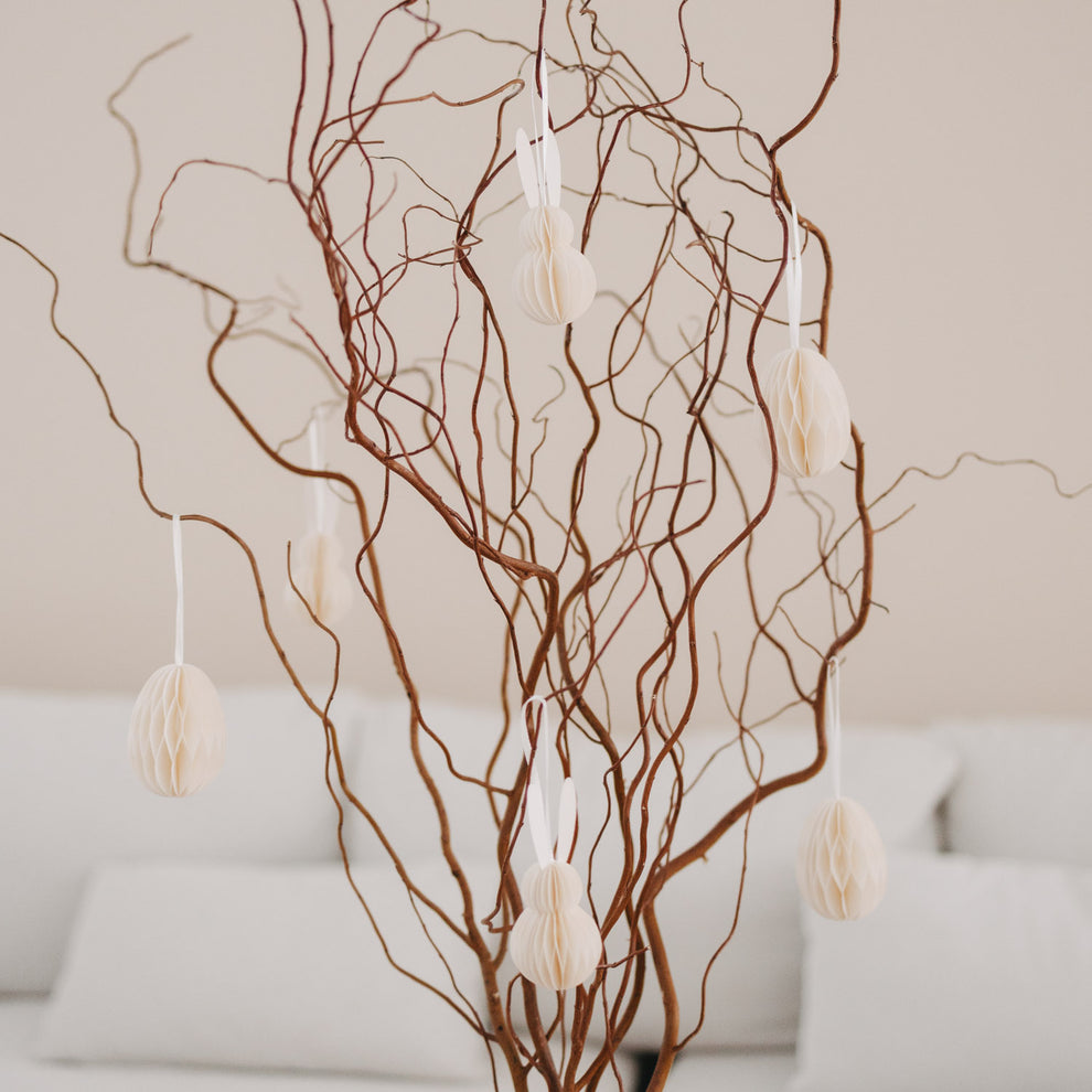 Beige Papieranhänger in Ei- und Hasenform an dekorativen Zweigen im Wohnzimmer.