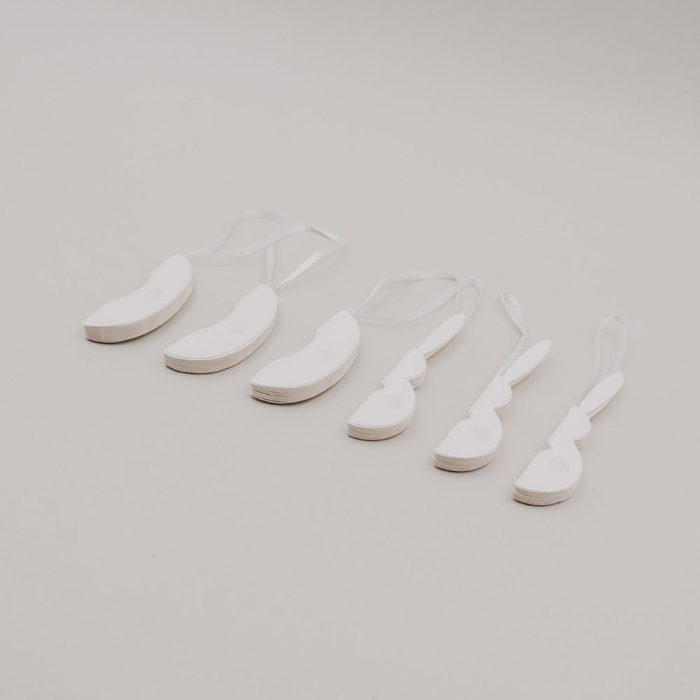 Flach gefaltete beige Papieranhänger in Ei- und Hasenform mit Bändern.