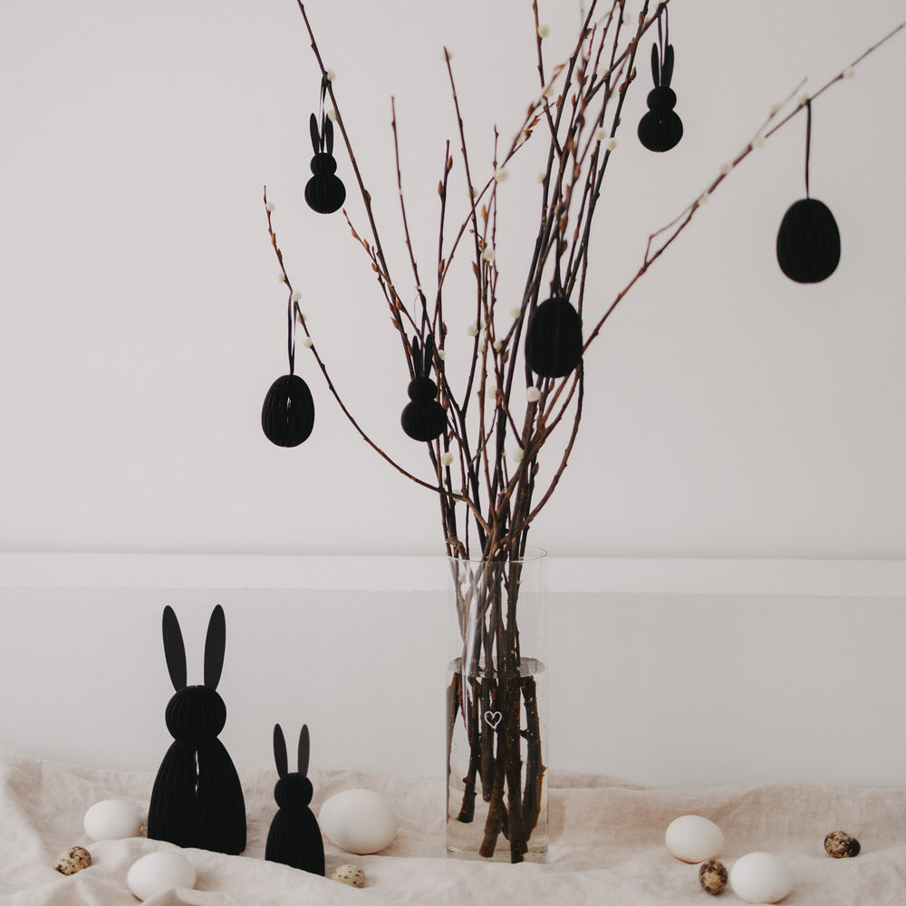 Schwarze Papierhasen und Osteranhänger an Zweigen als stilvolle Osterdekoration.