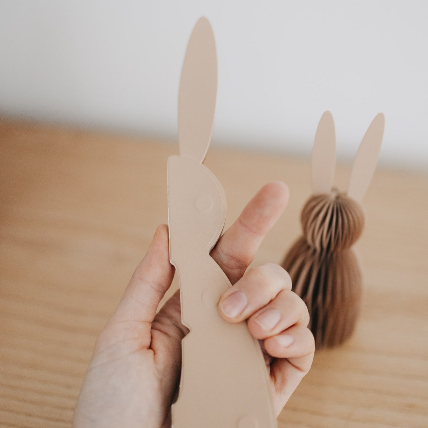 Naturfarbener Papierhase im Detail, gehalten in der Hand, flache Seitenansicht des Dekohasen.