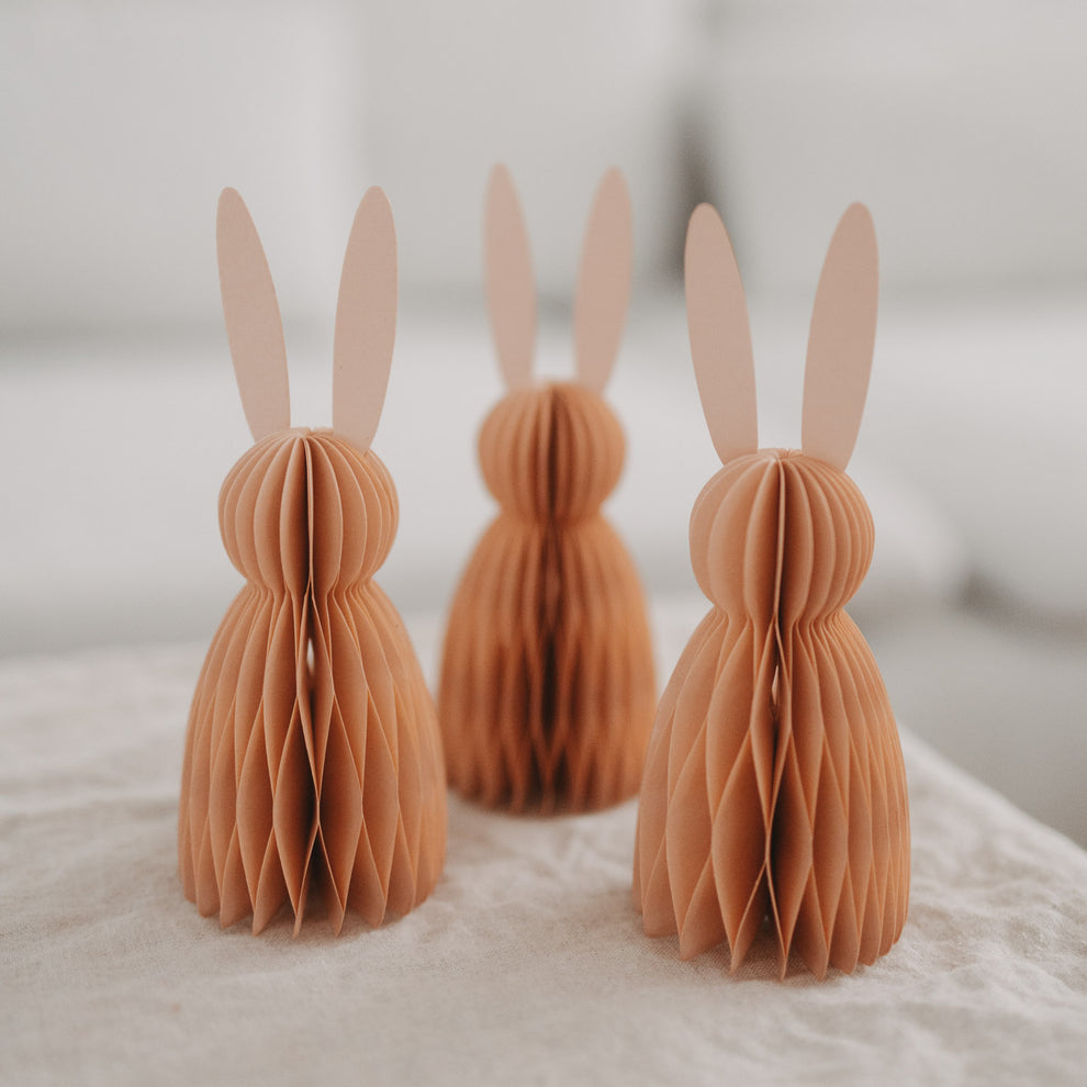 Drei peachfarbene Papierhasen im Honeycomb-Design als Osterdeko auf hellem Tisch arrangiert.
