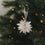 Naturfarbene Papierschneeflocke als Christbaumschmuck wird an den Weihnachtsbaum gehängt