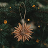 Braune Papierschneeflocke als filigraner Weihnachtsanhänger am Tannenzweig