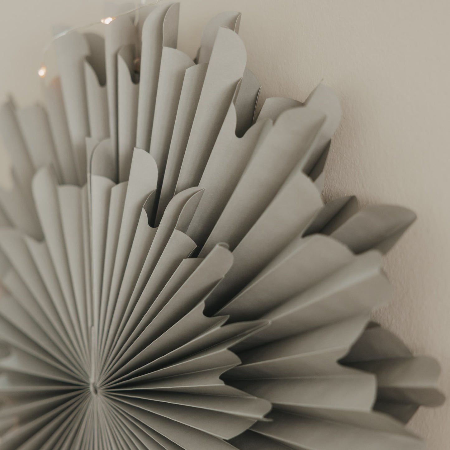 Graue Papierschneeflocke 45 cm als festliche Wanddekoration mit feinen Falten und Lichterkette
