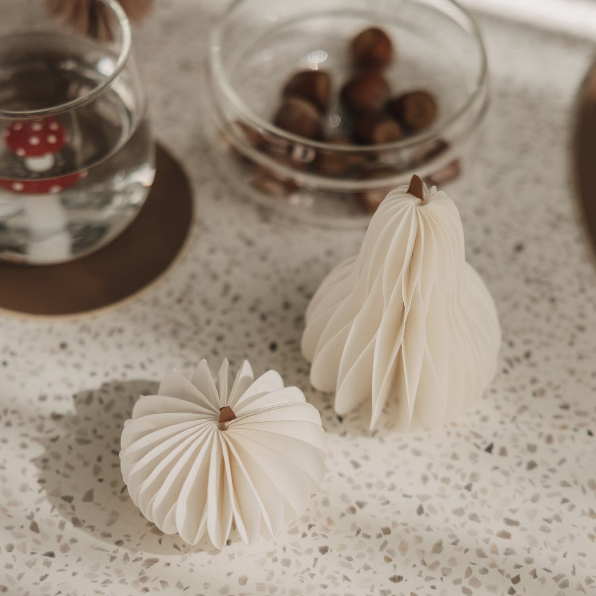 Zwei kleine weiße Papierkürbisse mit feiner Faltstruktur als minimalistische Herbstdeko